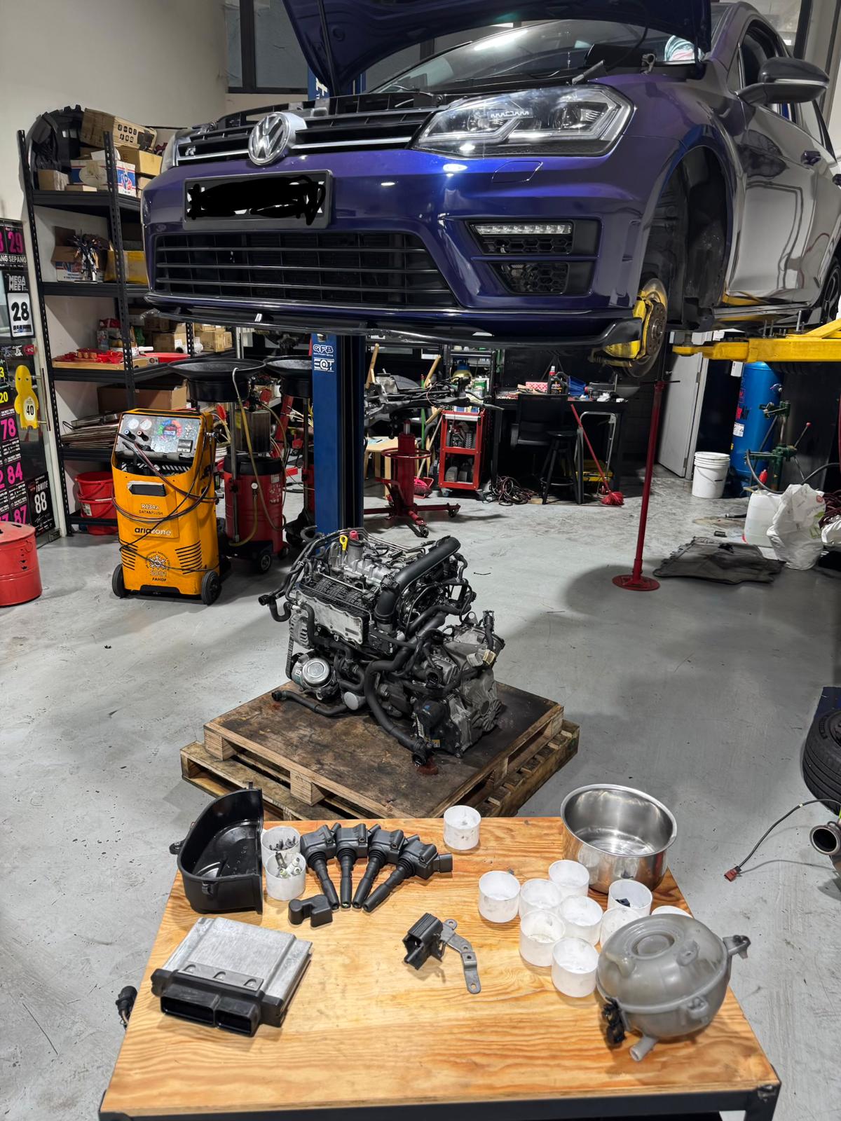 Volkswagen Golf MK7 on lift at TEC AUTO SERVICES with engine, coil packs, spark plugs, and ECU laid out on parts bench during an independent workshop diagnostic