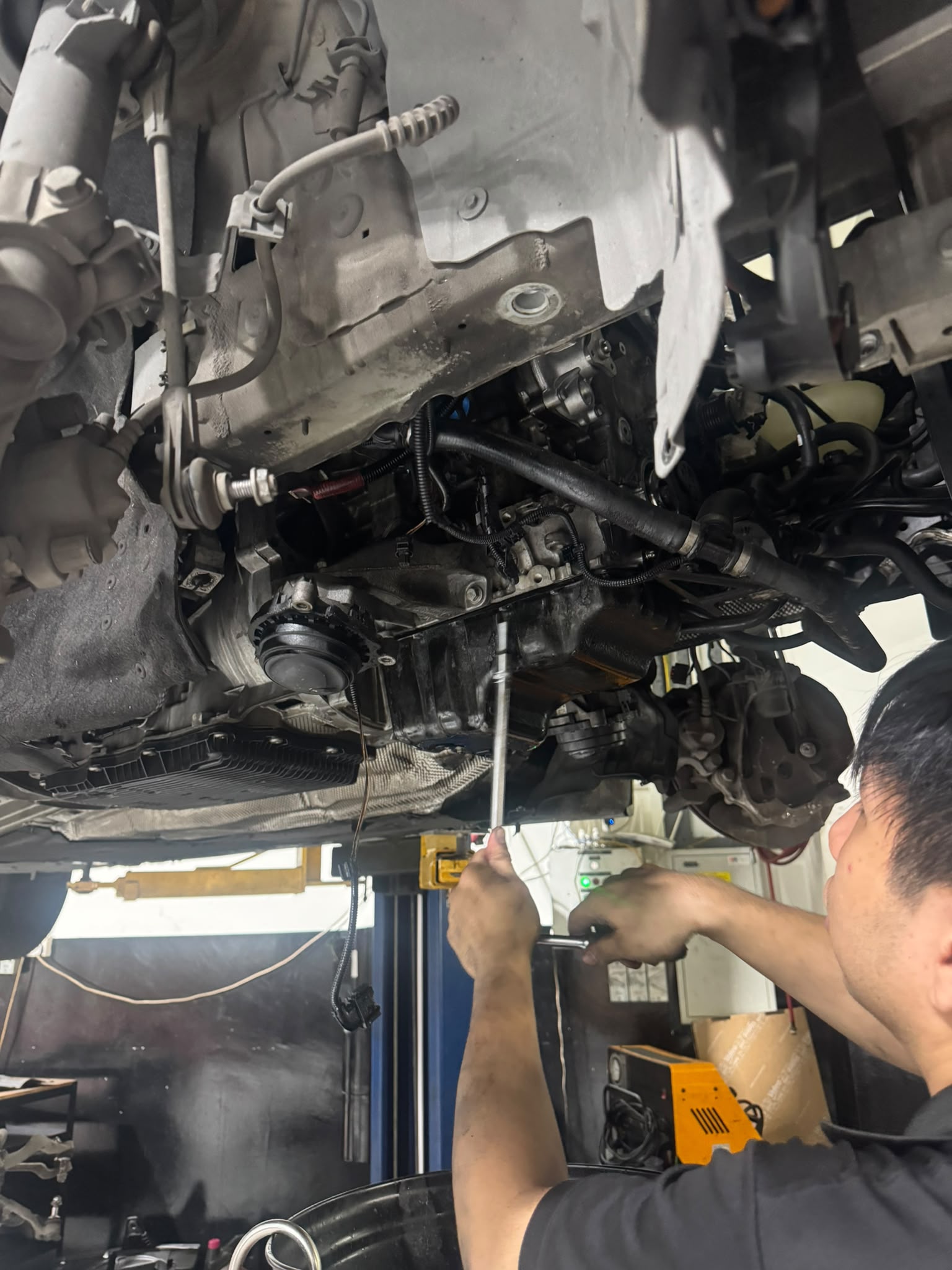 Technician draining gearbox fluid from underneath a BMW at a Singapore workshop in Woodlands